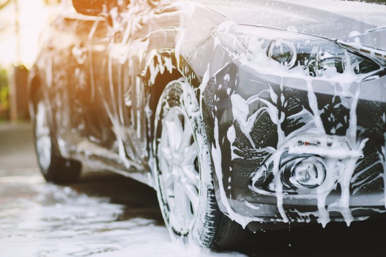 A grey-silver car covered in soap suds, at a car wash or car detailing.