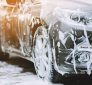 A grey-silver car covered in soap suds, at a car wash or car detailing.