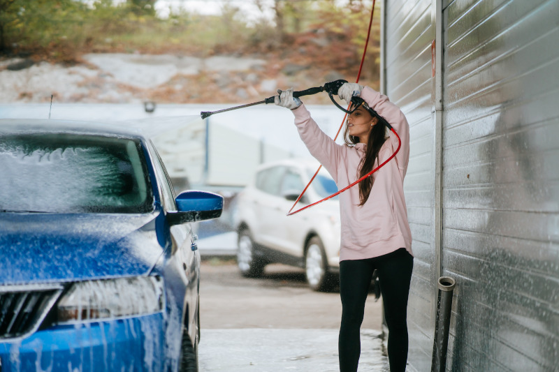 Young woman washing car at car wash